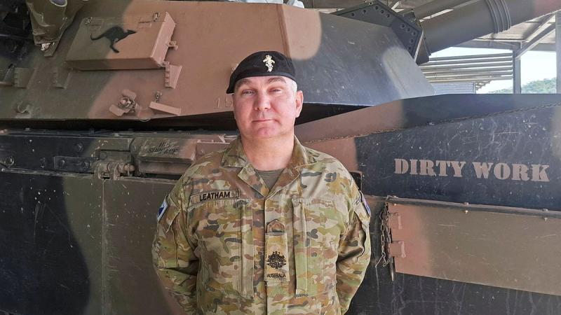 A soldier in uniform stands in front of an Army vehicle.
