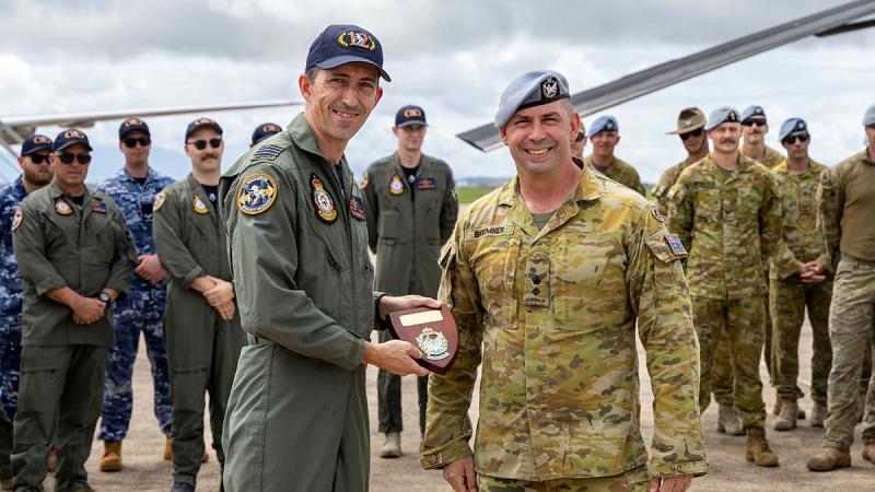 A man gives a plaque to another man while surrounded by a group of military personnel.
