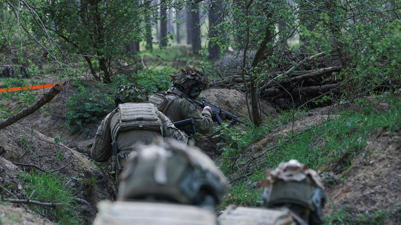 Military personnel crawl through trenches.