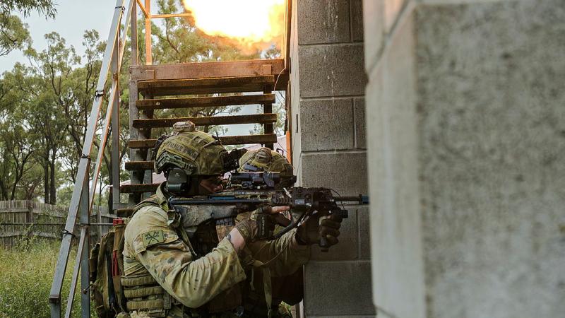 Soldiers breach the doorway of a building in flames.