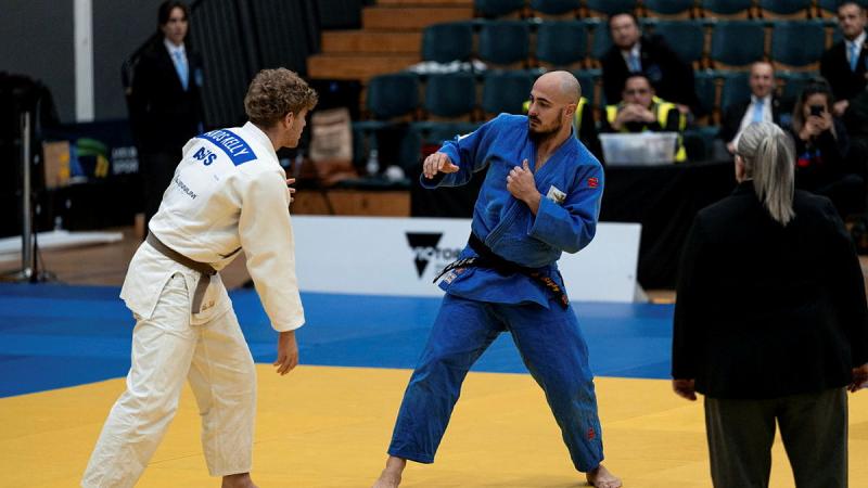 Two judo competitors shape up against each other in a stadium with a referee in the foreground.