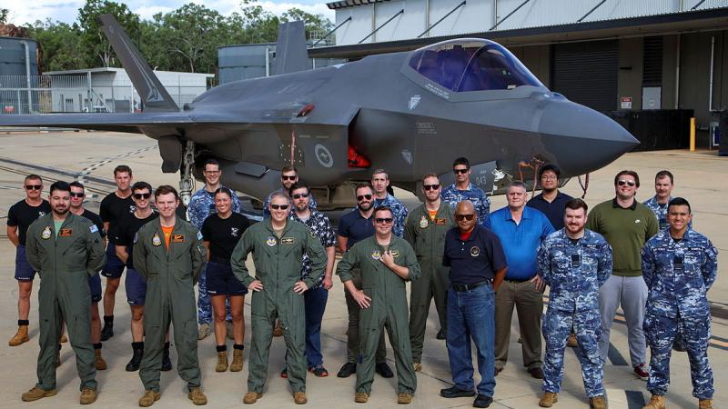 Military personnel stand before a stationary aircraft.