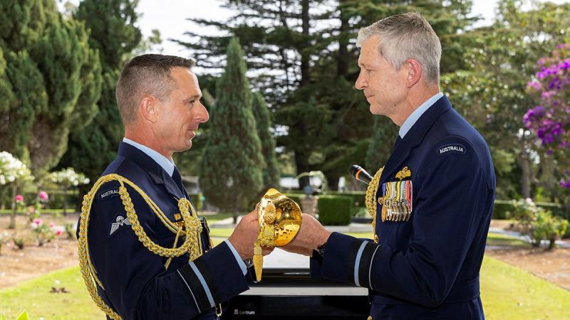 A man in formal military attire passes a sword to another man.