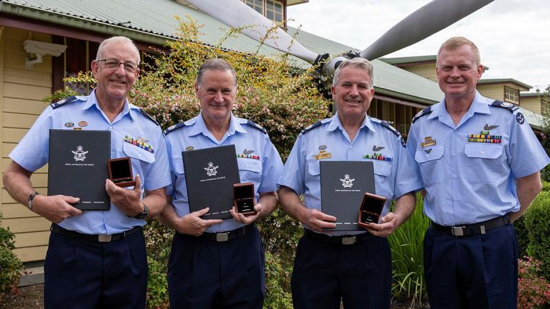 Four Air Force personnel stand holding awards in front of an aircraft propeller.