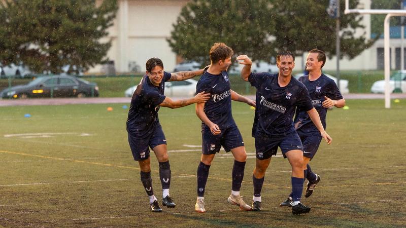 Four soccer players congratulate each other in the rain.