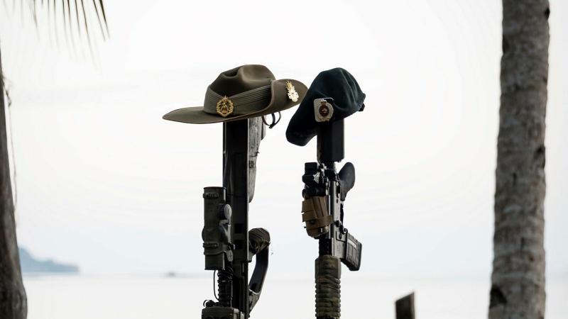 A slouch hat and beret placed atop two guns on a table with boots and sand bags.