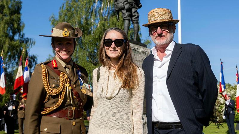 A military woman stands with two civilians at a formal service outside. 