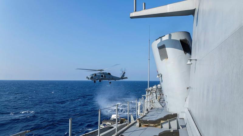 A helicopter flying low over the ocean water close to a ship.