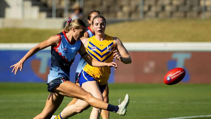 A woman kicks a football during an Aussie rules game.