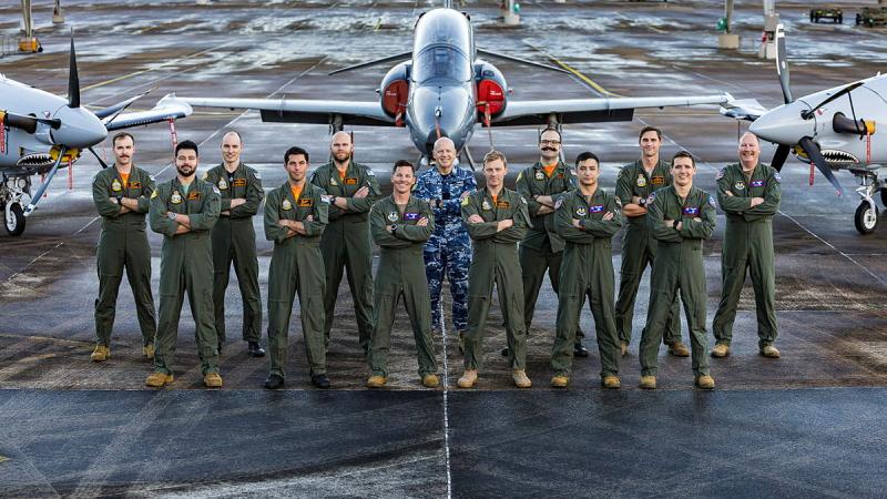 Group photo of pilot students and instructors on the tarmac in front of aircraft.