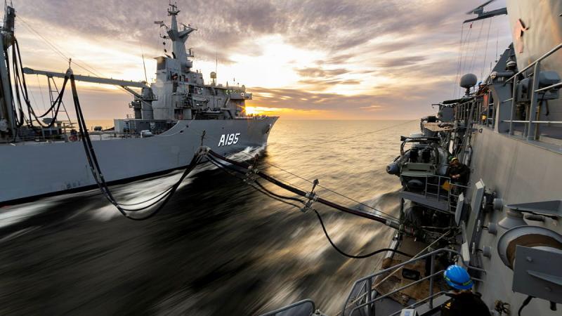 Two ships are connected by fuel lines while sailing together.