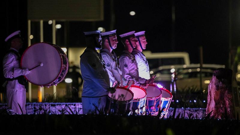 Navy personnel in uniform stand in low light with their drums.
