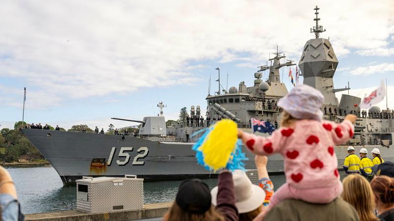 Families and friends stand looking at a ship, waving to members on board.