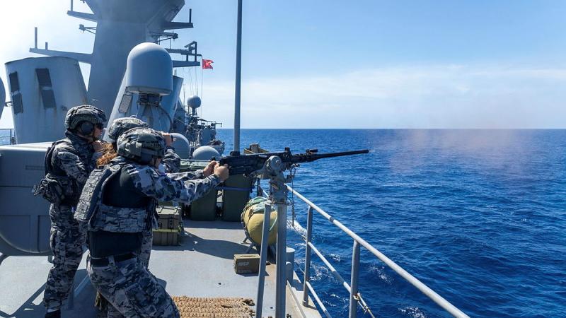 A group of sailors fire a machine gun from a ship.