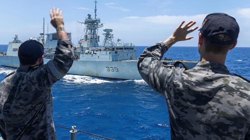 Navy personnel wave goodbye to another ship at sea.