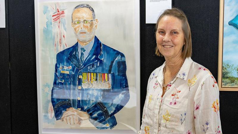 Royal Australian Air Force aviator Flight Sergeant Karen Tate-Smith stands with her portrait 'Devotion to Duty' at the 2026 Defending the Arts exhibition at the Australian Defence Force Academy.