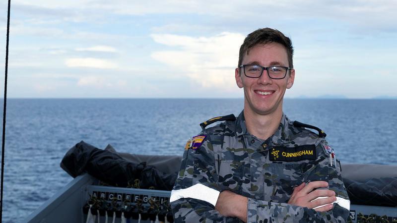 A man stands on a ship with his arms folded.