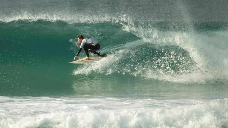 A male surfer rides an aqua blue waves with lots of spray coming off it.