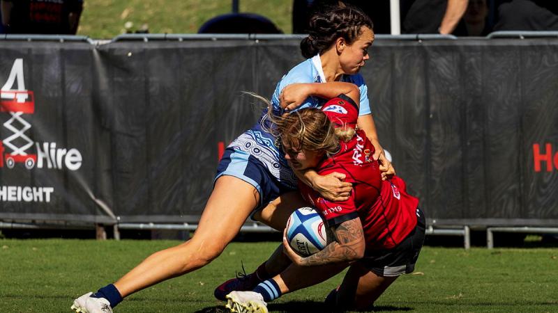 A female rugby player tackles another female rugby player during a game.