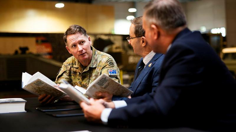 Three men sit at a table, each holding a book.