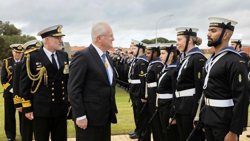 Navy personnel stand in line as they are inspected by two officials.