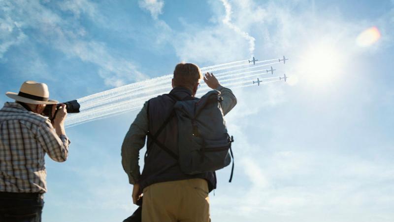 Two photographers watch five aircraft arch across the sky.