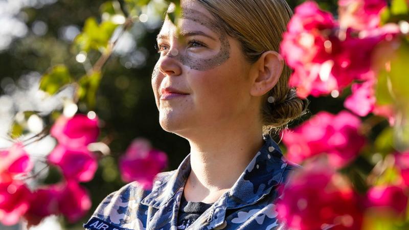 A woman with face paint standing amongst pink flowers.
