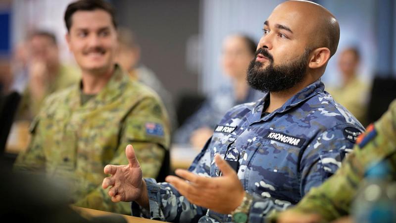 A man in Air Force uniform speaking to a group of people while sitting.