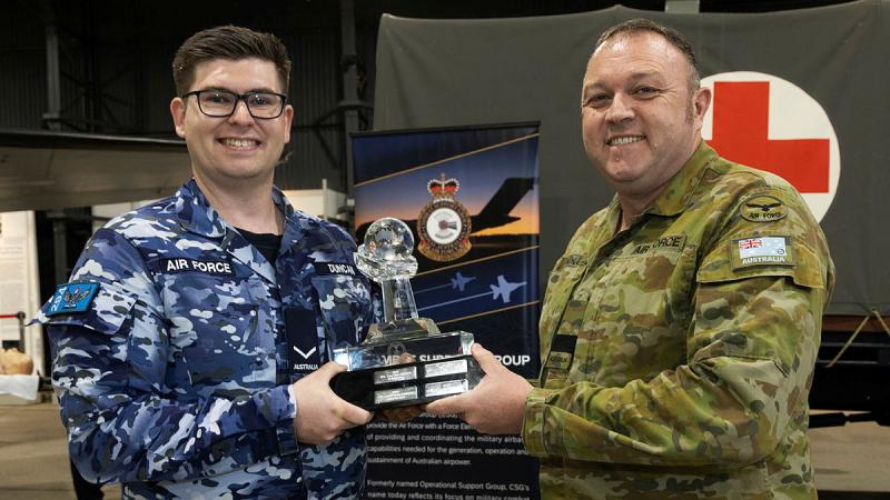 A man in Air Force uniform accepts a trophy from a man in Army uniform.