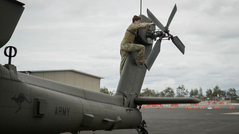 An Army pilot climbs up the tail of a helicopter on the tarmac.
