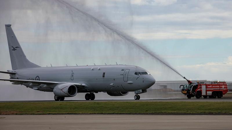A hose from a firetruck shoots water over an aircraft on the tarmac.
