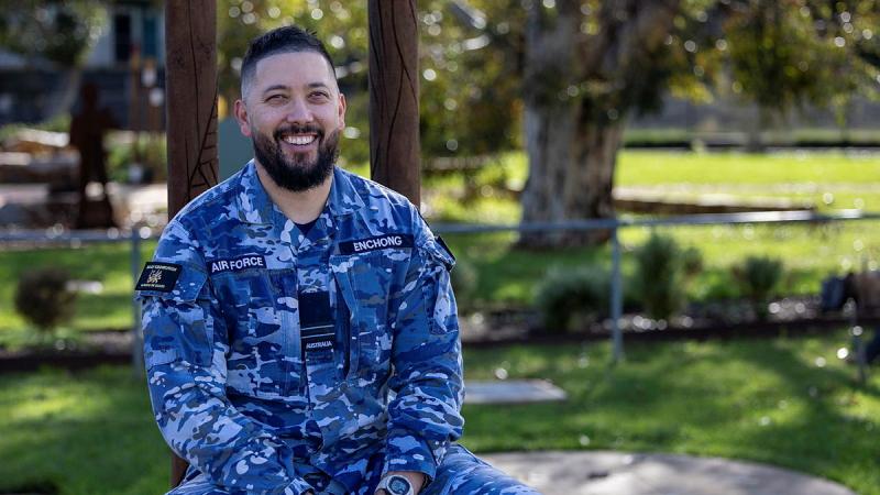 A military man sits on a bench outside.