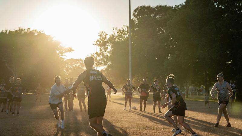 People playing rugby outside as the sun sets.