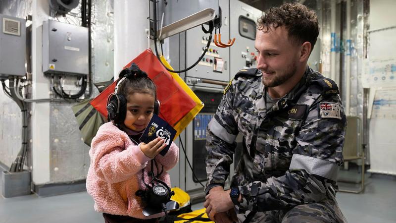 A sailor shows equipment to a child wearing headphones.