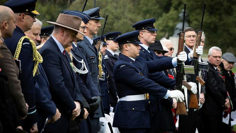 Armed military personnel stand in formation with civilians.