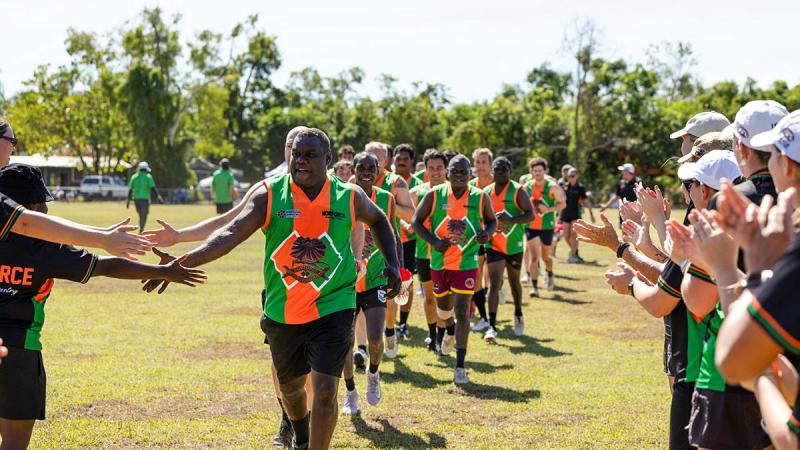 A sports team runs out onto the field and high fives spectators. 