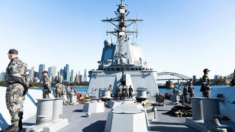 Sailors line the upper decks of a ship. 