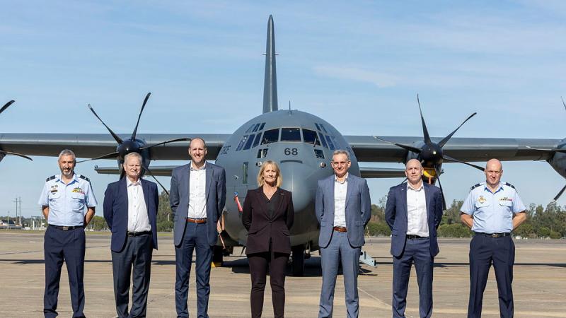 Seven people stand in a line in front of an aircraft on the tarmac.