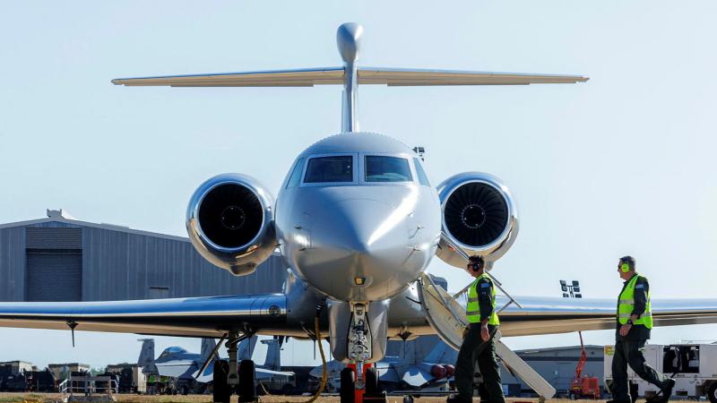 Two military members walk towards a stationary aircraft on the tarmac.