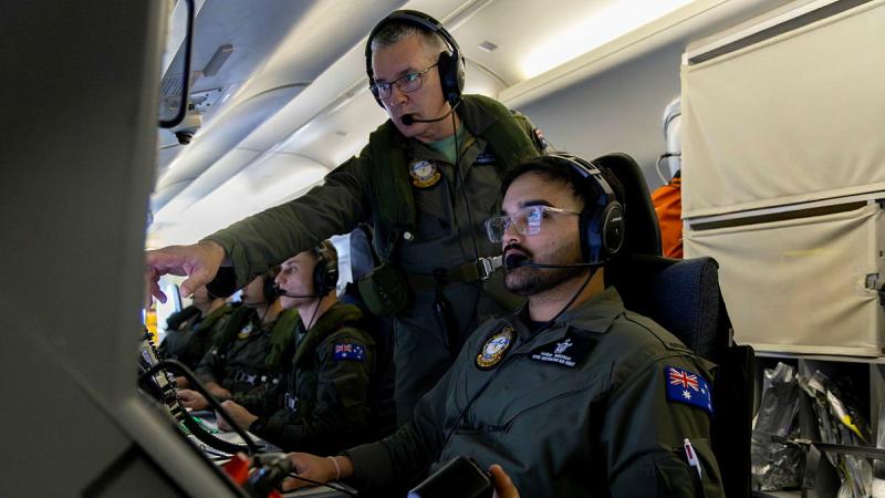 A military member points at the screen of another military member while inside an aircraft.