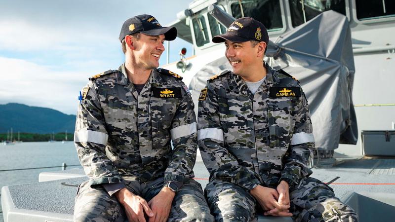 Two men sit and smile at each other. 
