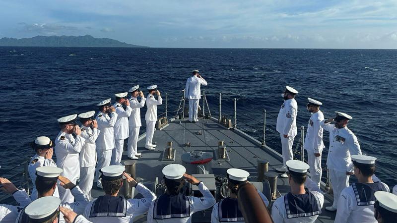 Sailors stand and salute on a boat at sea.
