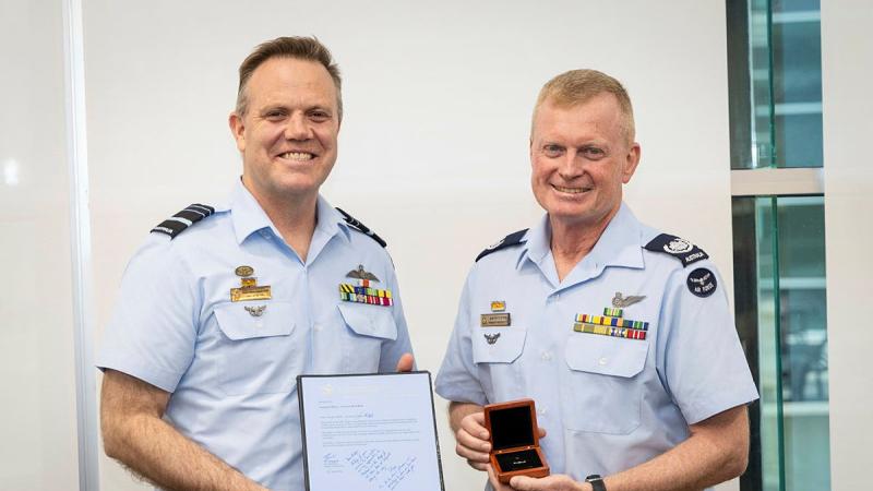 Two men in Air Force uniform stand holding awards and smiling at the camera.