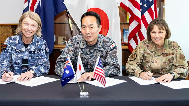 Three military personnel from Australia, Japan and the US all sign a document each.