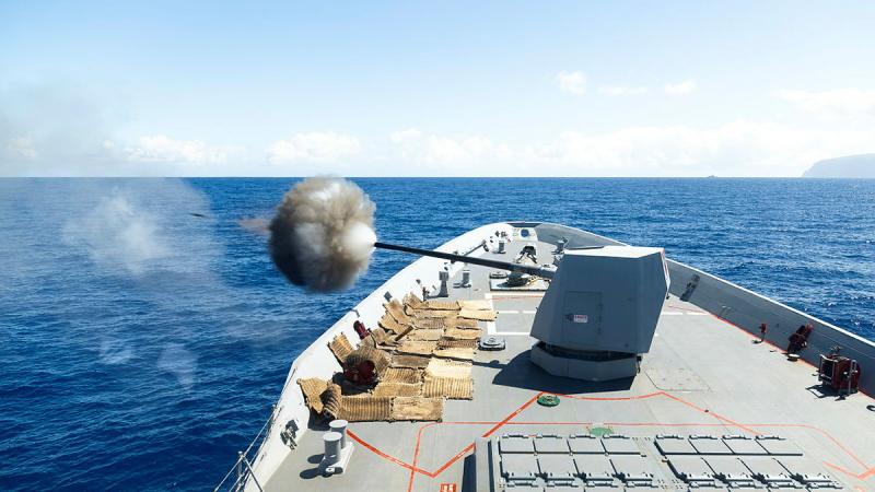 A gun fires from a ship at sea.