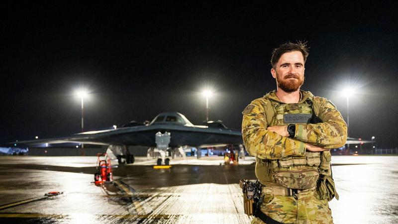 A man in military uniform stands on the tarmac in front of an aircraft.
