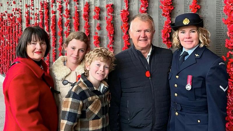 A group of people standing together in front on a memorial wall of poppies. 