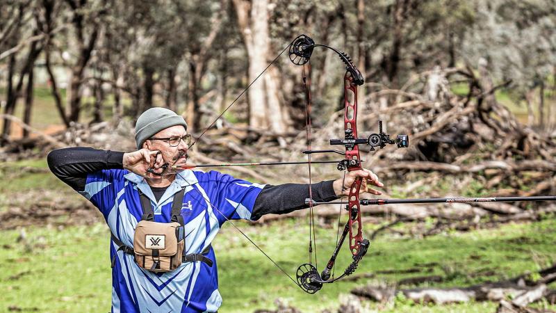 A man with a bow takes aim out in the wilderness.