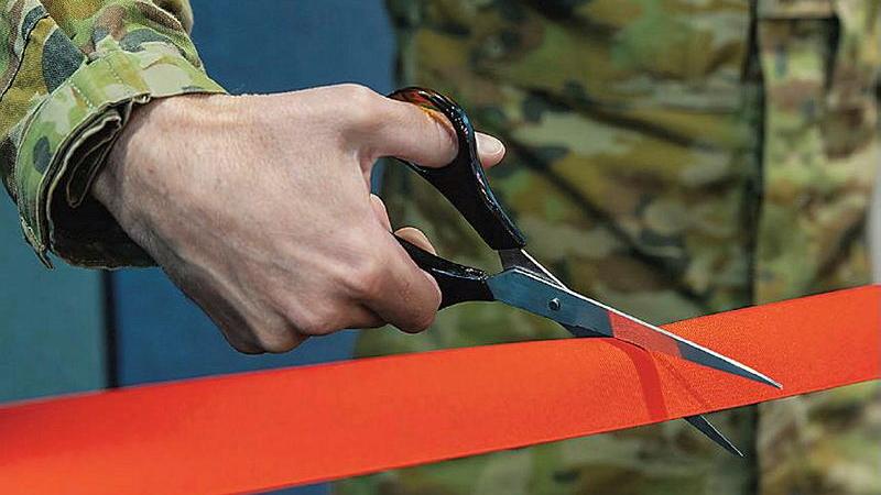 A soldier's hand holds scissors cutting a red tape.