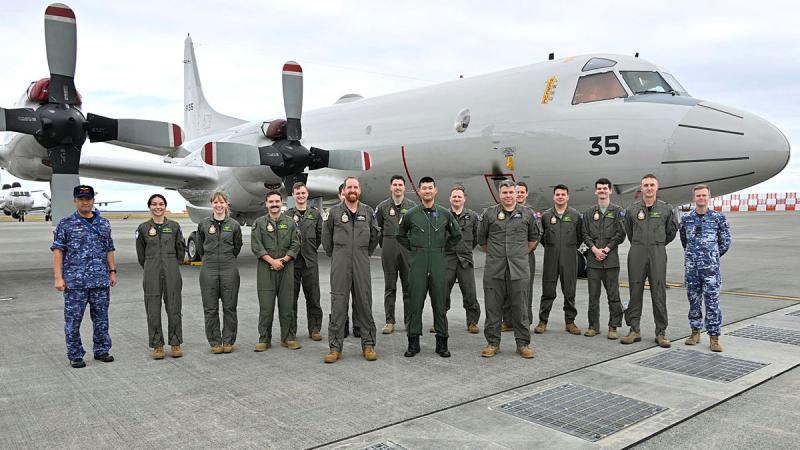 A group of military personnel stand in front of an aircraft on the tarmac.